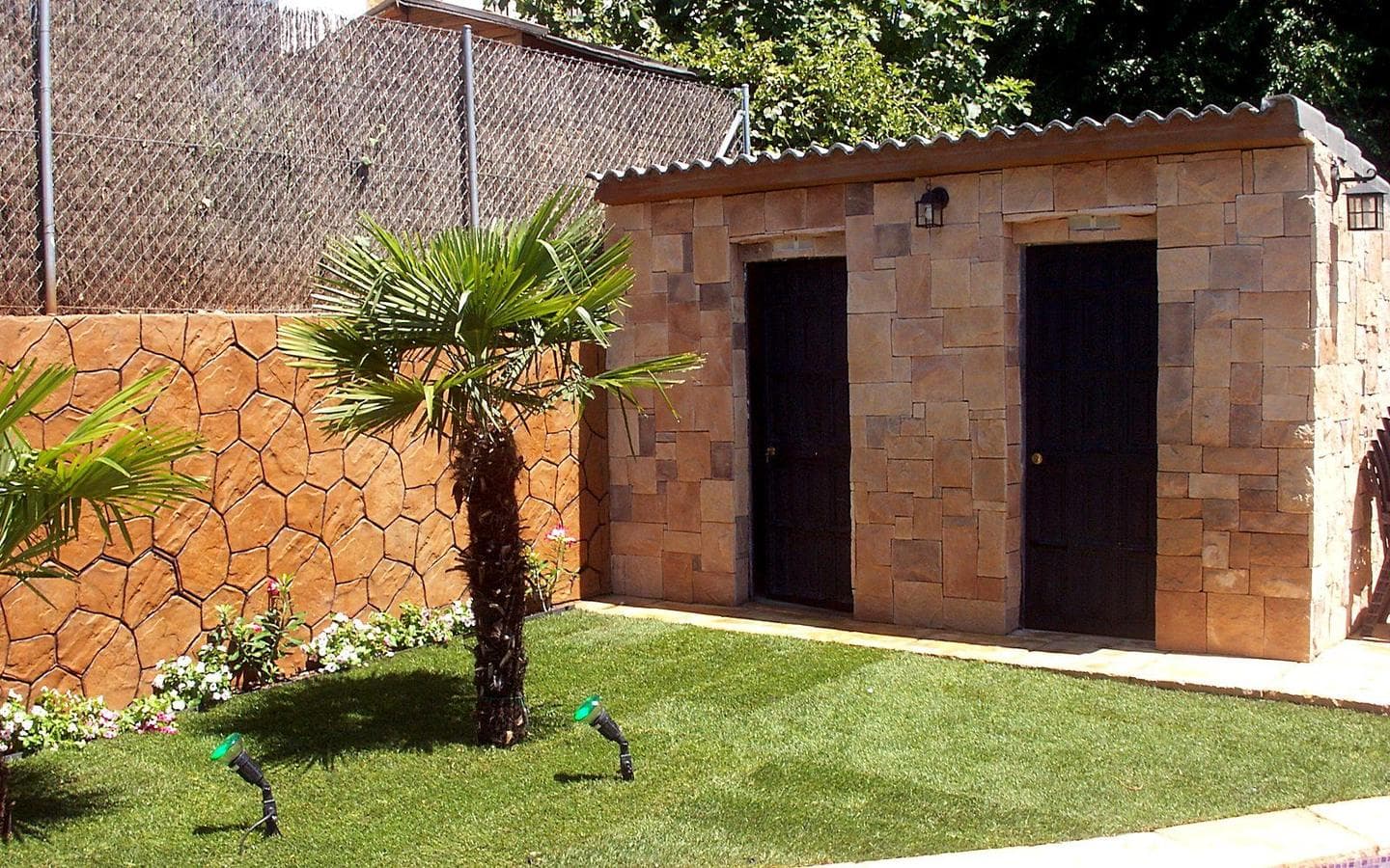 Caseta de piedra con dos puertas, una para la sala de máquinas y otra para el baño, junto a una palmera y césped